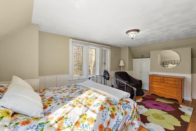 bedroom featuring vaulted ceiling, wood finished floors, and a wainscoted wall