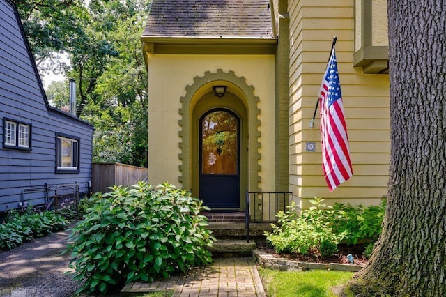 view of exterior entry with fence and a shingled roof