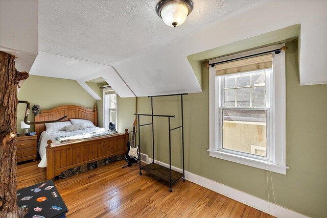 bedroom with lofted ceiling, hardwood / wood-style flooring, baseboards, and a textured ceiling