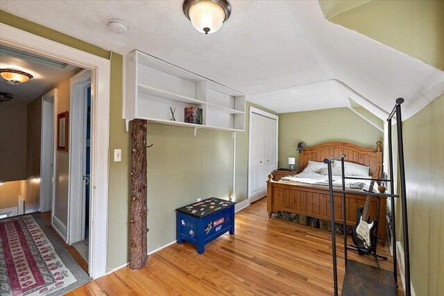 bedroom featuring a closet, a textured ceiling, lofted ceiling, and wood finished floors