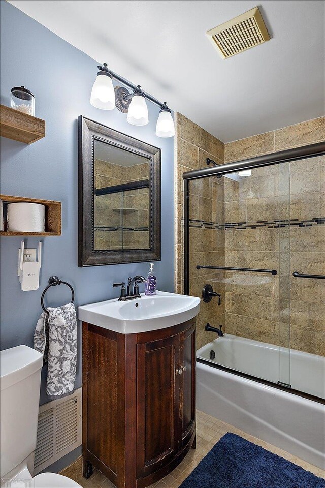 full bath featuring visible vents, toilet, vanity, and bath / shower combo with glass door