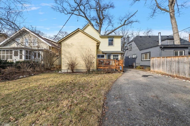 rear view of property with a deck, a lawn, fence, and driveway