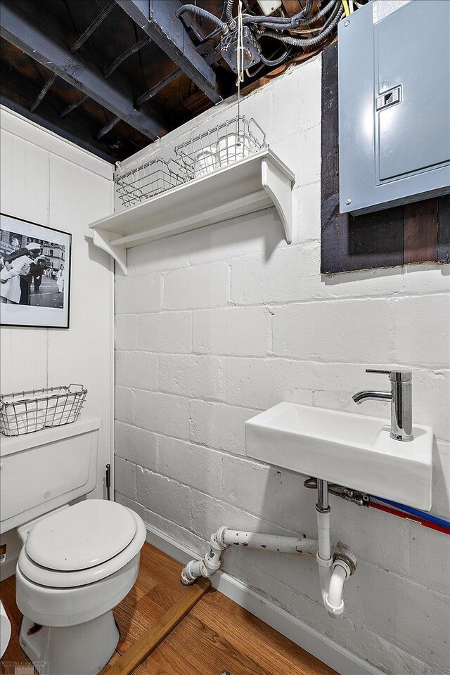 half bath featuring electric panel, toilet, concrete block wall, and a sink