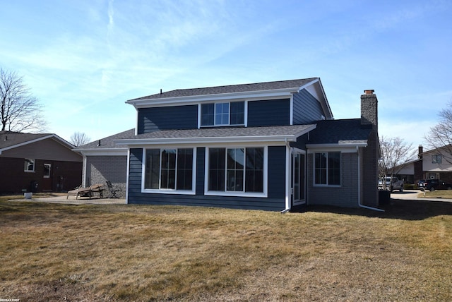 rear view of property featuring a shingled roof, a yard, brick siding, and a chimney