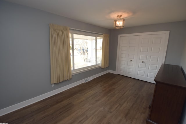 unfurnished bedroom with dark wood-style floors, visible vents, a closet, and baseboards