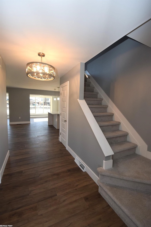 stairway featuring visible vents, an inviting chandelier, baseboards, and wood finished floors