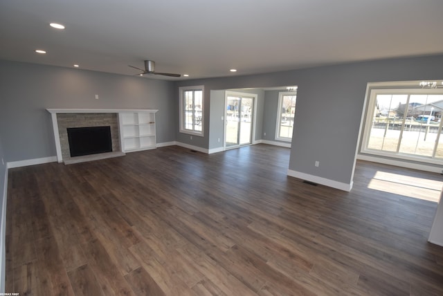 unfurnished living room featuring dark wood-style floors, recessed lighting, a fireplace with raised hearth, and baseboards