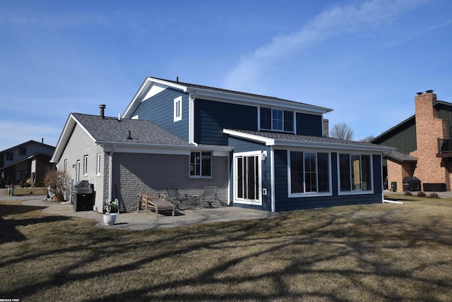 rear view of house featuring a patio, a sunroom, a shingled roof, a lawn, and brick siding