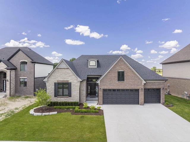 french country home featuring driveway, stone siding, roof with shingles, a front yard, and brick siding