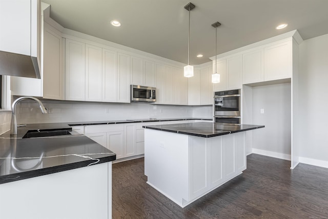 kitchen with dark countertops, a sink, appliances with stainless steel finishes, white cabinetry, and dark wood-style flooring