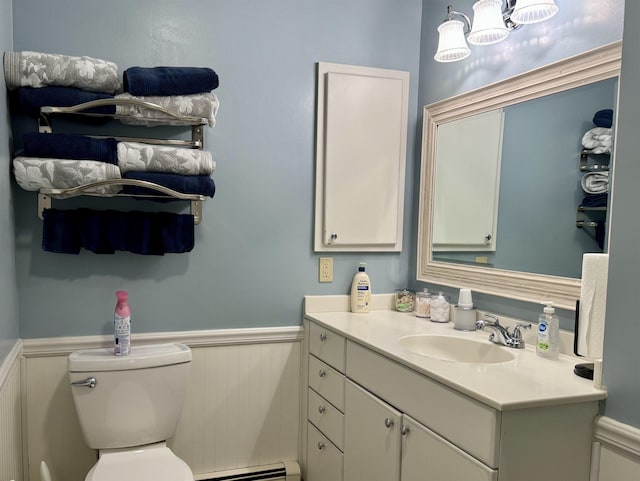 half bath with a wainscoted wall, toilet, vanity, and baseboard heating