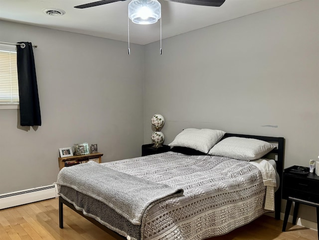 bedroom with wood finished floors, visible vents, baseboard heating, and ceiling fan