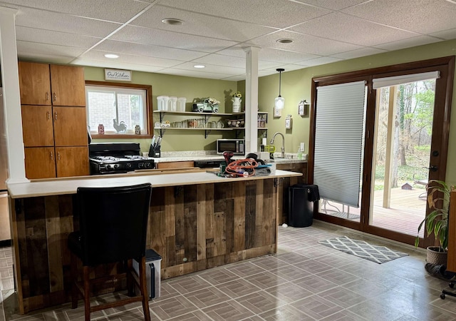 bar with stainless steel microwave, black gas stove, a paneled ceiling, and a sink