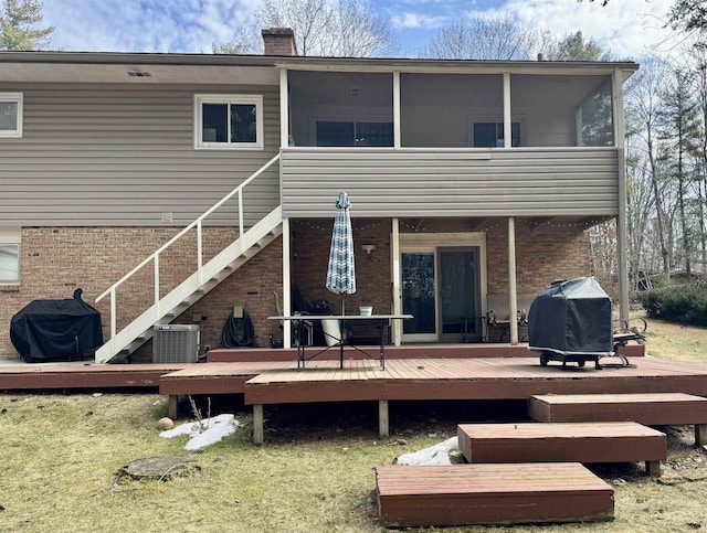 rear view of property featuring stairway, a sunroom, a chimney, a deck, and brick siding