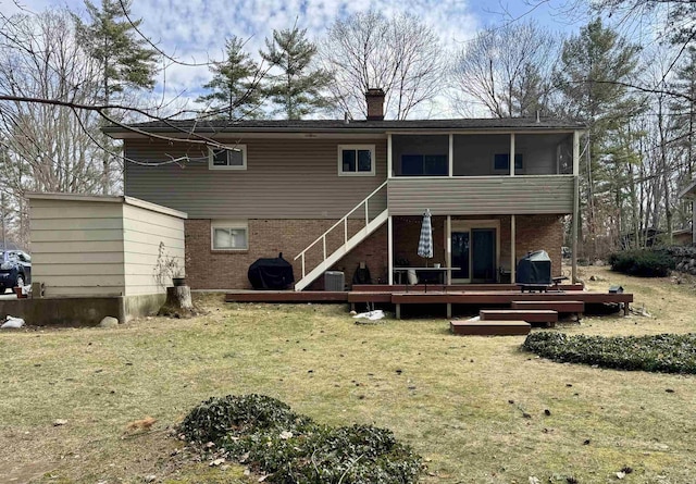 rear view of house featuring brick siding, a chimney, a wooden deck, and a sunroom