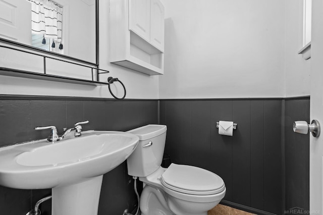 half bath featuring toilet, a wainscoted wall, and a sink