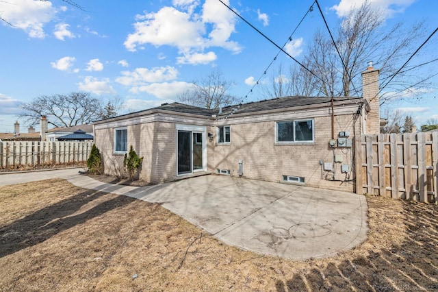 rear view of property featuring a patio, brick siding, a chimney, and fence