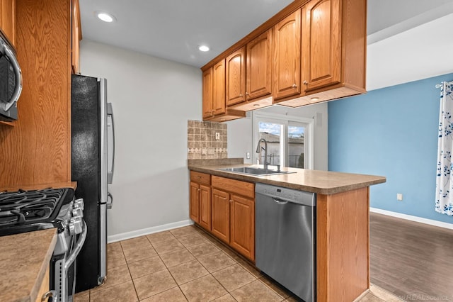 kitchen featuring baseboards, a peninsula, a sink, decorative backsplash, and stainless steel appliances