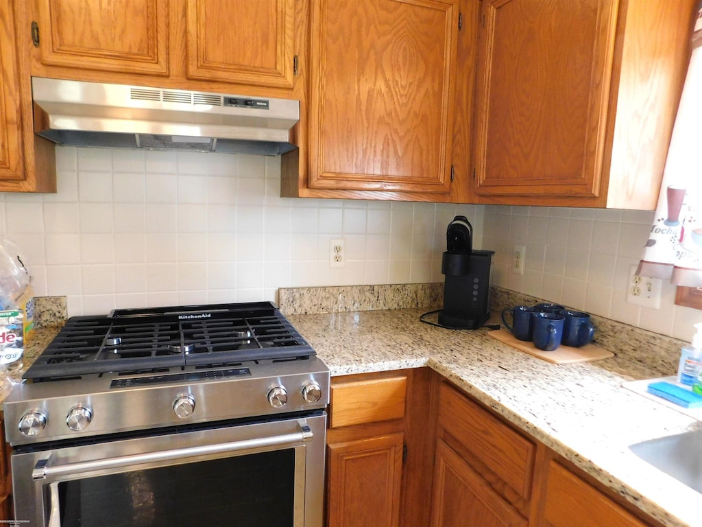 kitchen with gas stove, decorative backsplash, under cabinet range hood, and brown cabinetry