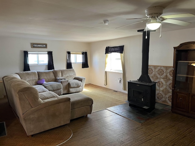 living area with a wood stove, wood finished floors, visible vents, and ceiling fan