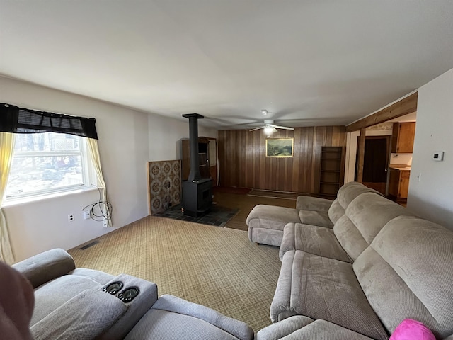 living area with visible vents, wooden walls, a wood stove, and a ceiling fan