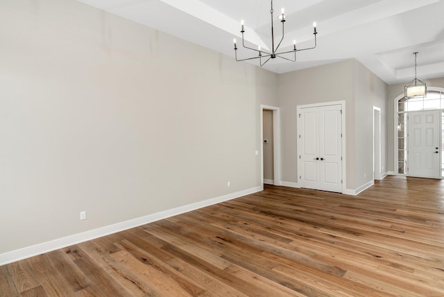 interior space with a raised ceiling, a notable chandelier, wood finished floors, and baseboards