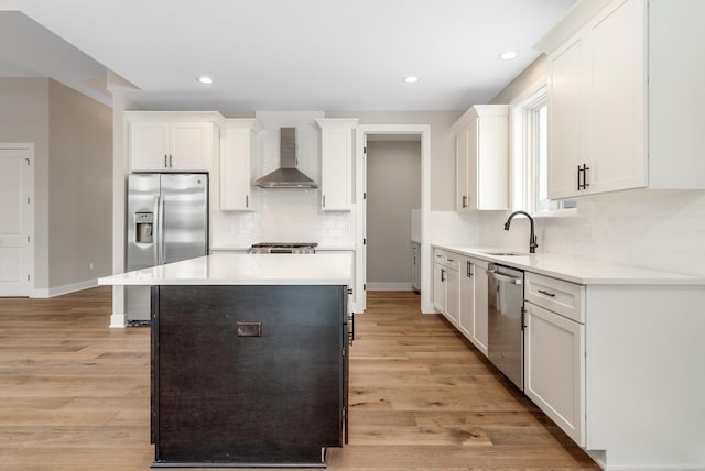 kitchen featuring light wood-type flooring, a sink, a kitchen island, appliances with stainless steel finishes, and wall chimney exhaust hood