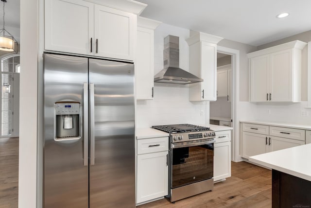 kitchen with light wood-style floors, appliances with stainless steel finishes, wall chimney exhaust hood, white cabinets, and light countertops