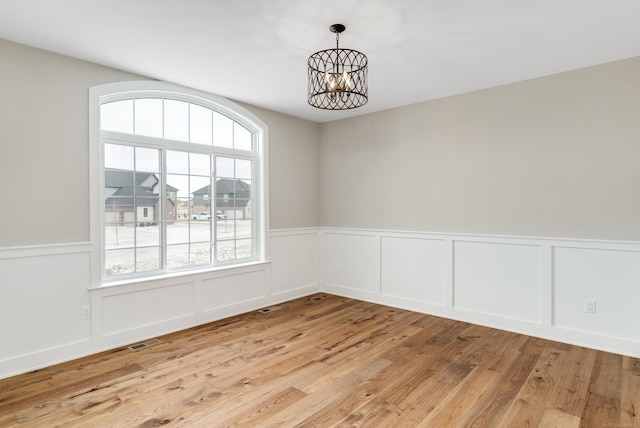 unfurnished room with a notable chandelier, visible vents, light wood finished floors, and a wainscoted wall