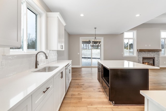 kitchen with tasteful backsplash, dishwasher, light wood-type flooring, a stone fireplace, and a sink