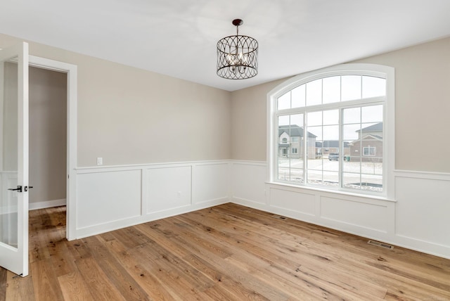 spare room featuring an inviting chandelier, visible vents, light wood finished floors, and wainscoting