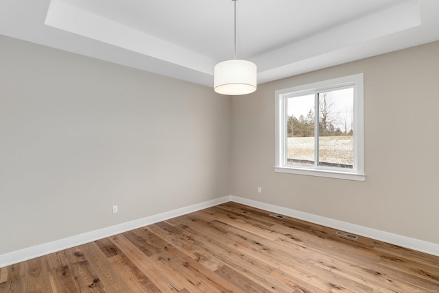 spare room with a tray ceiling, baseboards, and wood finished floors