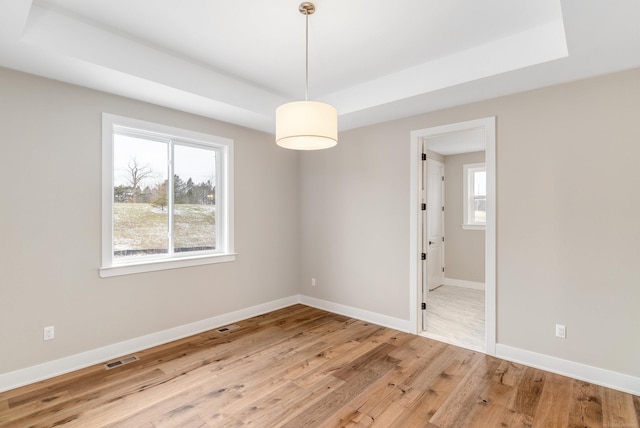 spare room featuring a tray ceiling, light wood-type flooring, baseboards, and visible vents