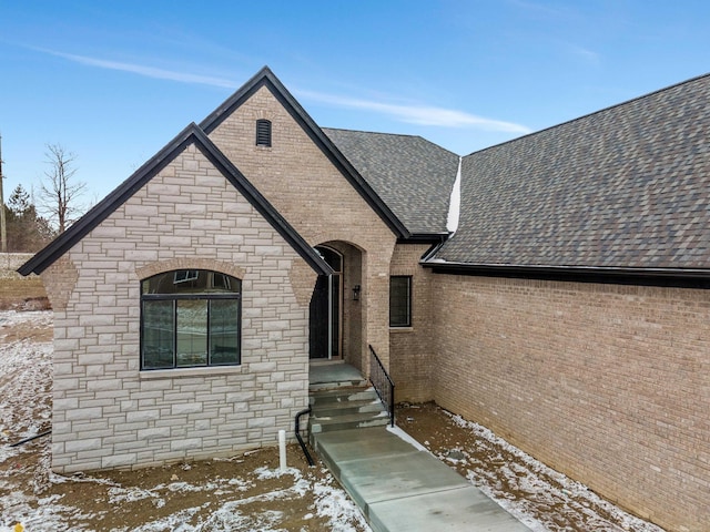 view of front facade with stone siding, brick siding, and a shingled roof