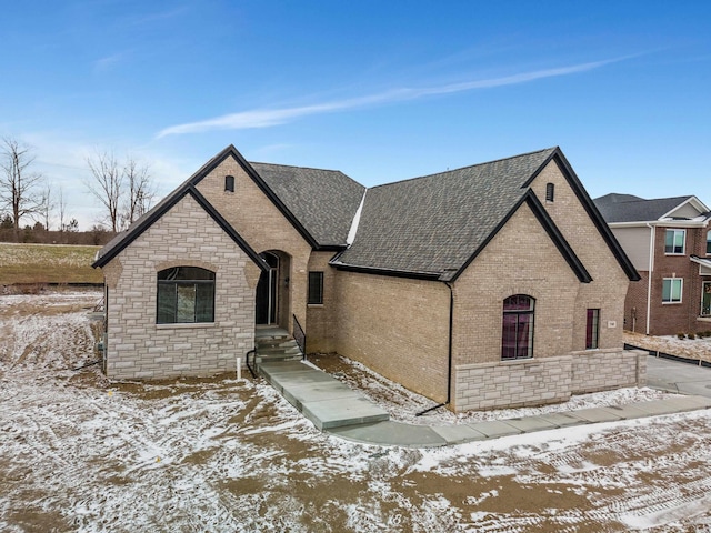 french country home featuring brick siding, stone siding, and a shingled roof