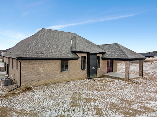 rear view of house with brick siding, a patio area, cooling unit, and a shingled roof