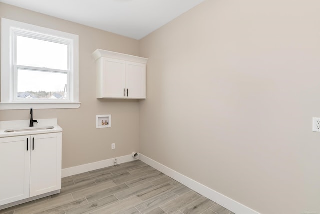 washroom featuring washer hookup, a sink, cabinet space, light wood-style floors, and baseboards