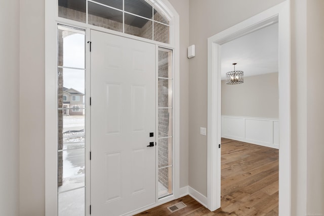 foyer entrance with a wainscoted wall, visible vents, dark wood-type flooring, a decorative wall, and a notable chandelier