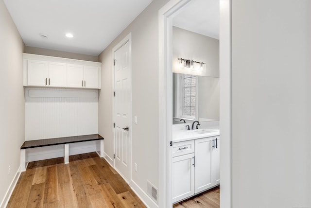 mudroom featuring light wood-style flooring, baseboards, visible vents, and a sink