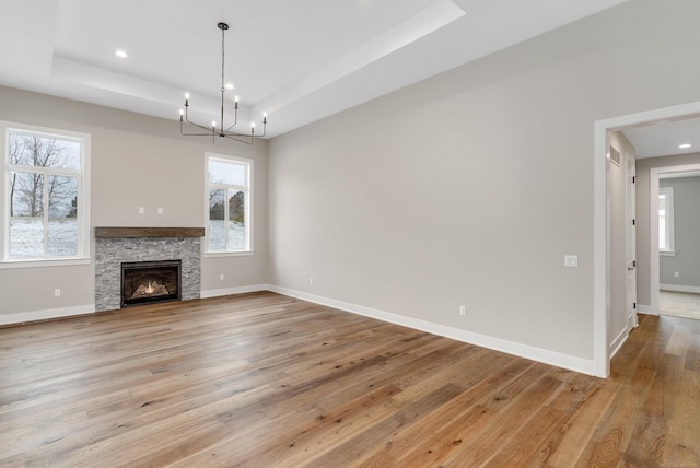 unfurnished living room featuring baseboards, an inviting chandelier, a tray ceiling, recessed lighting, and light wood-type flooring