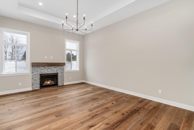 unfurnished living room featuring a raised ceiling, a notable chandelier, baseboards, and light wood finished floors