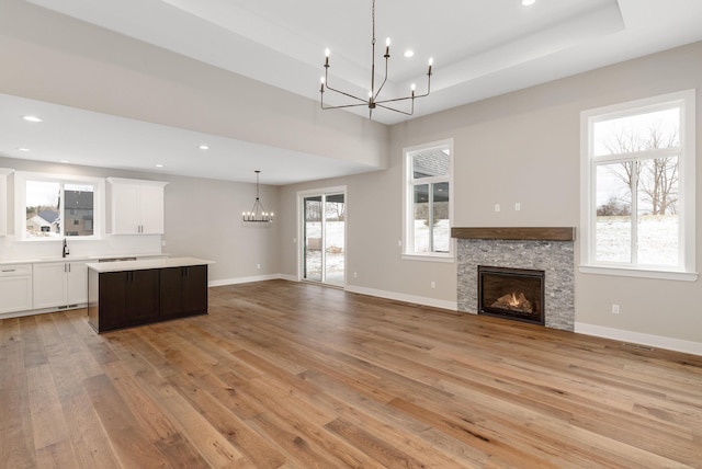 interior space featuring a notable chandelier, a kitchen island, light wood-style floors, a stone fireplace, and light countertops