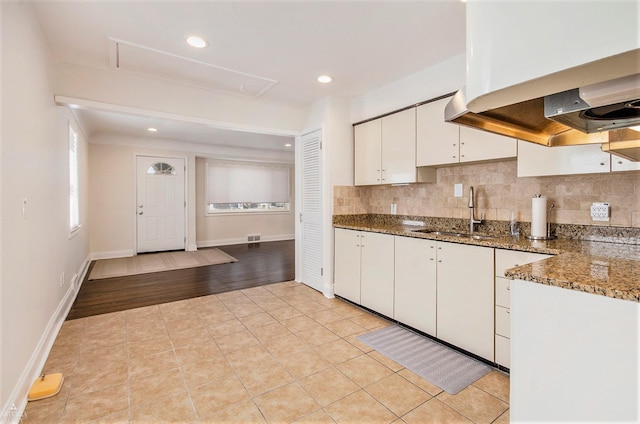 kitchen with decorative backsplash, range hood, white cabinets, and a sink