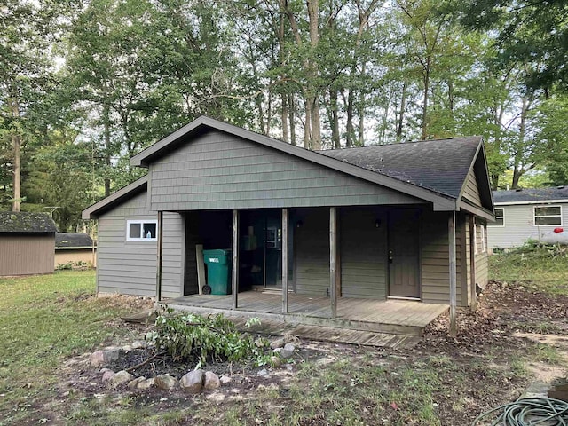 rear view of house featuring roof with shingles, an outdoor structure, and a shed