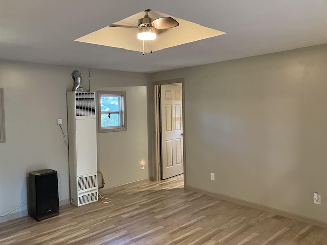 unfurnished room featuring a ceiling fan, light wood-style floors, a heating unit, and baseboards