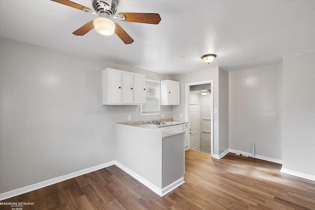 kitchen featuring baseboards, wood finished floors, light countertops, and white cabinetry