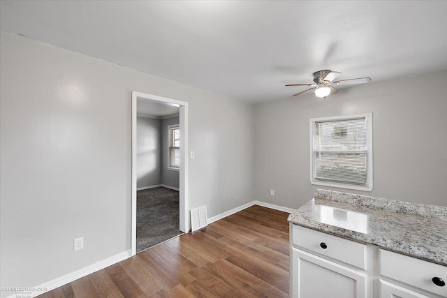 interior space with visible vents, baseboards, wood finished floors, white cabinets, and a ceiling fan