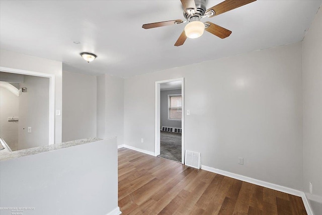 empty room featuring a ceiling fan, wood finished floors, visible vents, and baseboards