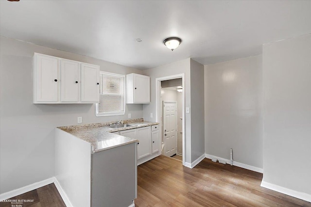 kitchen featuring white cabinetry, wood finished floors, baseboards, and a sink