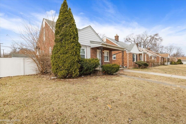 view of front of house featuring a front lawn, fence, brick siding, and a chimney